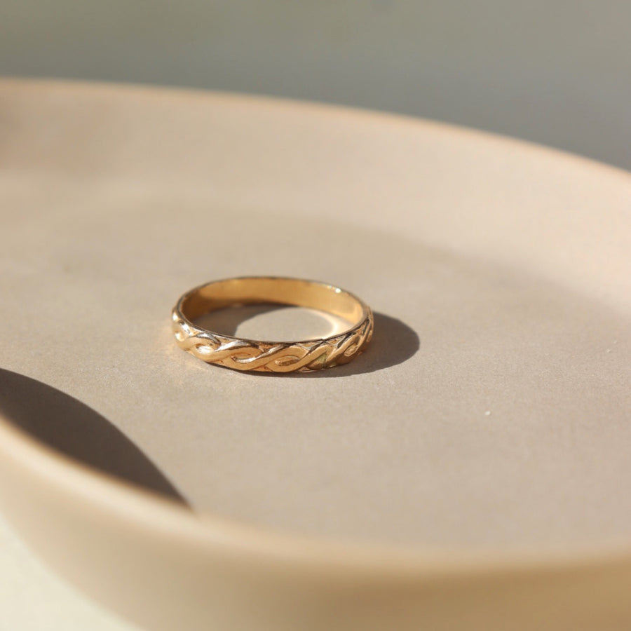 14k gold fill Helix run placed on a peach plate in the sunlight. This ring feature a small twist like band.