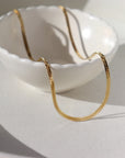 14k gold fill Luxe Herringbone Chain on a white bowl in the sunlight.