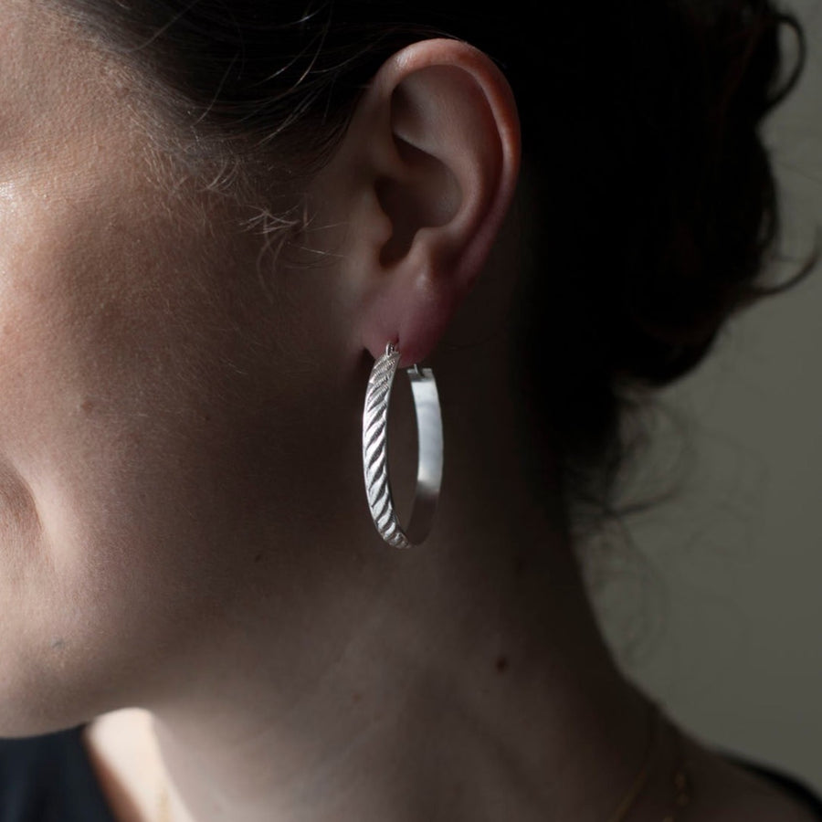 925 sterling silver hoop earrings, approximately 1.5" diameter with a soft ripple pattern engraved. they're photographed on a brunette model in shadow and sun