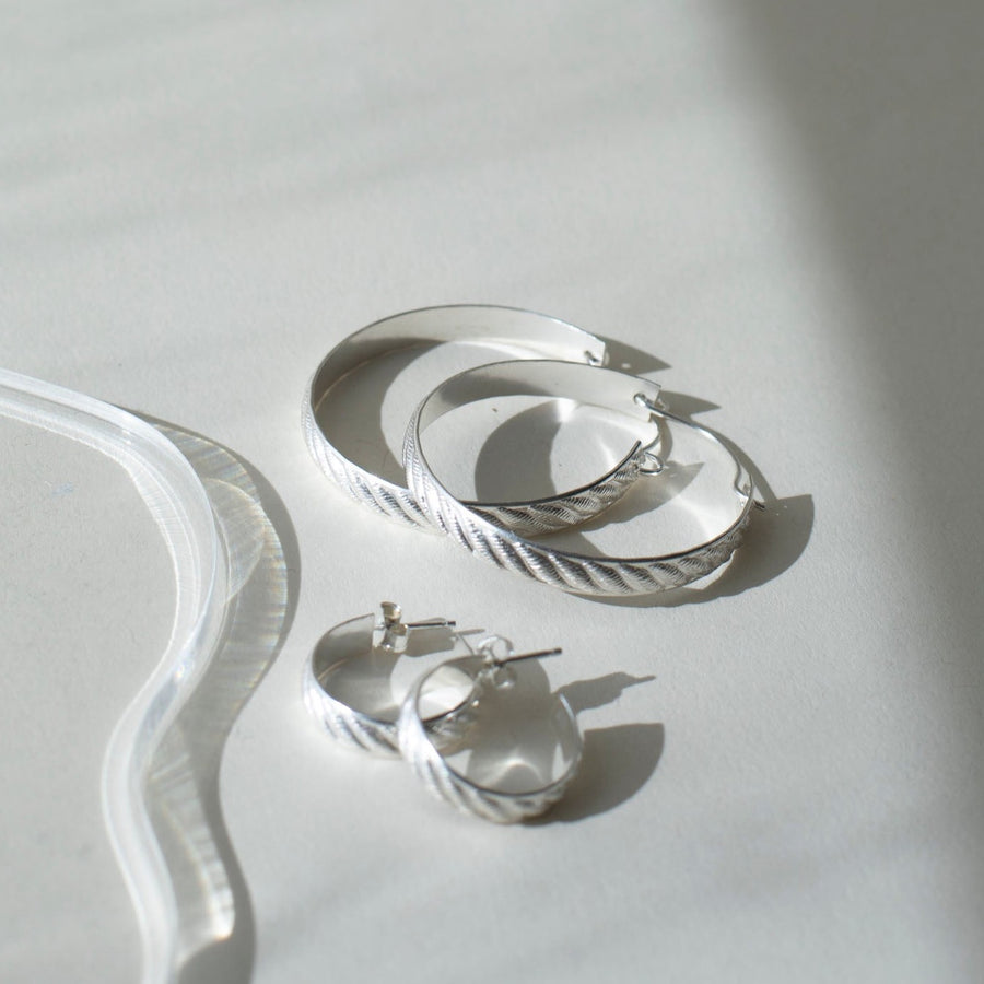 925 sterling silver hoop earrings, approximately 1.5" diameter with a soft ripple pattern engraved. they're photographed on a white table in the sunlight next to the little ripple hoops